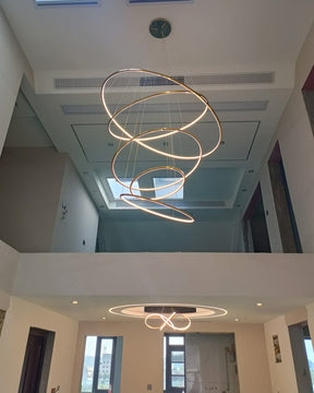 Long gold ring chandelier installed through a two-story opening, demonstrating how its adjustable drop can suit challenging ceiling heights.