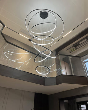 Shiny black entryway chandelier glowing above a mirrored stairwell, combining graphic contrast with airy, unobstructed sightlines.