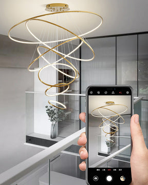 Golden LED chandelier viewed from an upper landing, revealing how the long cascading form connects multiple floors with one dramatic focal point.