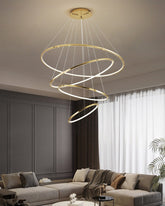 Four illuminated gold rings descending above a gray lounge, delivering statement lighting with a cleaner profile for moderately high ceilings.