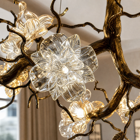 An antique brass chandelier with branching arms and frosted glass blossom shades suspended by cables.