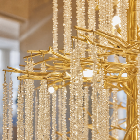 A large, multi-tiered chandelier with a gold branch-like frame and long strands of cascading crystal droplets.