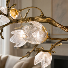 An antique brass chandelier with metal tree branches and frosted glass magnolia blossom shades suspended by multiple cables.