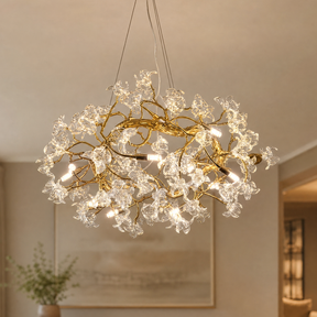 A modern organic chandelier features a warm antique brass branch frame decorated with twelve clear sculpted glass blossoms.
